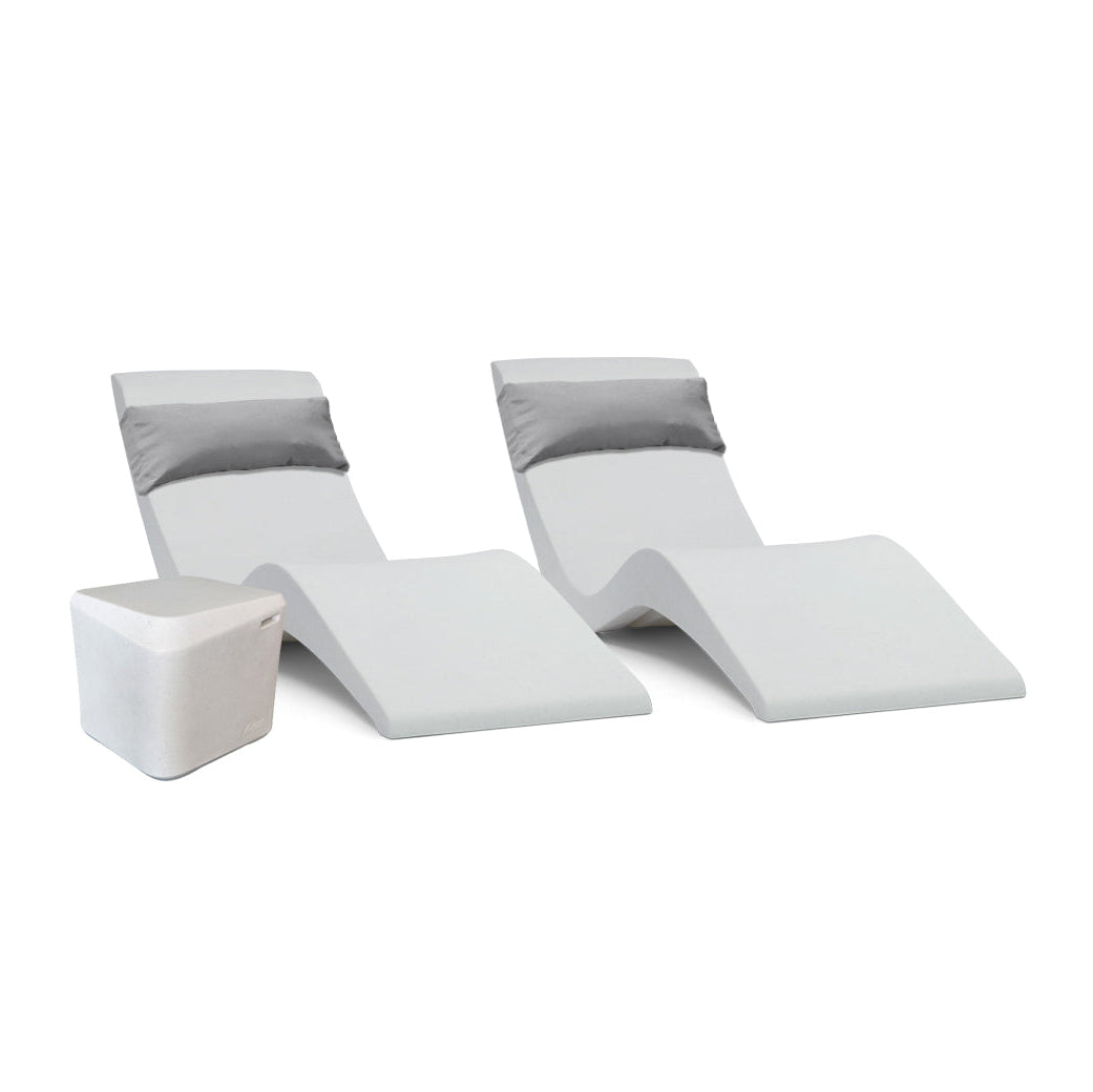 The Pool Lounge Chair Set by AquaOutdoors features two modern, minimalist chaise loungers with sleek curves and gray cushions paired side by side on a tanning shelf, accompanied by a small white cube-shaped side table. A plain white backdrop highlights the sets elegant design.