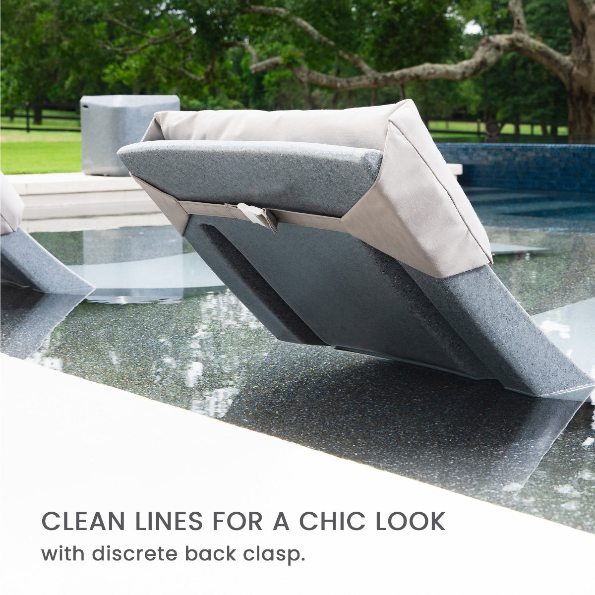 Modern outdoor seating featuring sleek cushions with a discreet back clasp, positioned on a smooth reflective surface. The background shows a green lawn and trees. Text reads: Clean lines for a chic look with discrete back clasp.