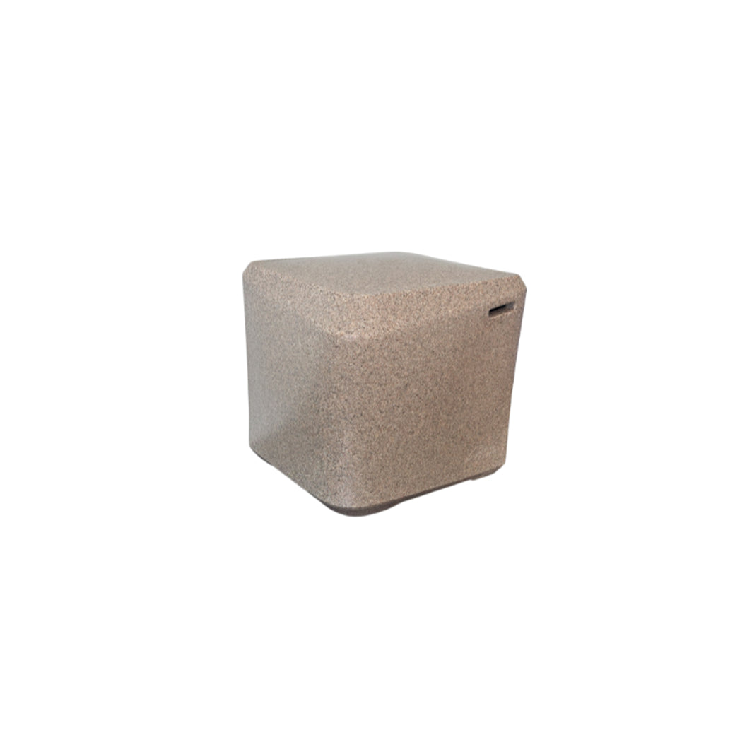 The AquaOutdoors In Pool Table, a compact light brown cube with rounded edges and textured surface, elegantly complements the serene look of pool lounge chairs on a sun-drenched deck against a plain white background.