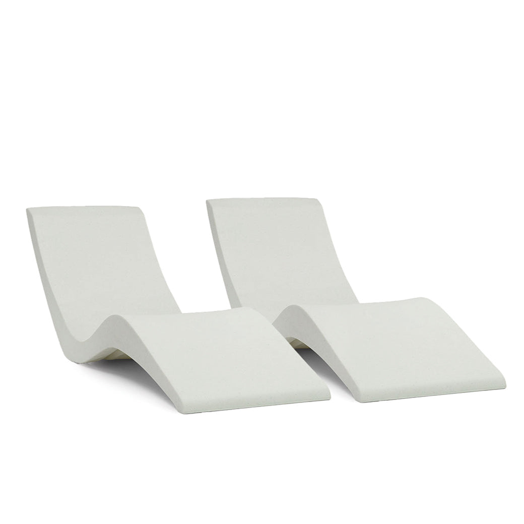 The Chaise Lounge Set by AquaOutdoors, featuring two modern wave-shaped chairs in solid surface material, is displayed against a plain white backdrop to highlight their minimalist design.